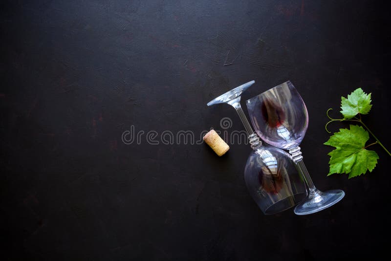 Two wineglasses with red wine, cork and grape leaves lying on dark wooden background. Top view. Flat lay. Copy space. Two wineglasses with red wine, cork and grape leaves lying on dark wooden background. Top view. Flat lay. Copy space