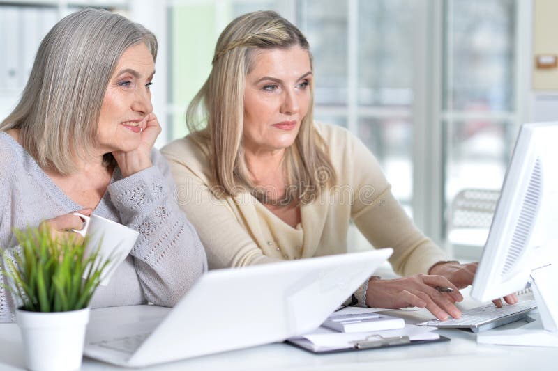 Two excited mature women working in office with modern devices. Two excited mature women working in office with modern devices