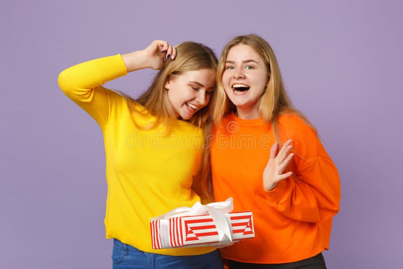 Dwa zaskakującej blondynka bliźniaków siostr dziewczyny w żywej ubrania chwyta czerwieni paskowali teraźniejszego pudełko z preze obraz royalty free Dwa zaskakującej blondynka bliźniaków siostr dziewczyny w żywej ubrania chwyta czerwieni paskowali teraźniejszego pudełko z preze obraz royalty free