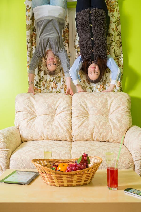 Two women stand upside down and hold on to the sofa. Two women stand upside down and hold on to the sofa