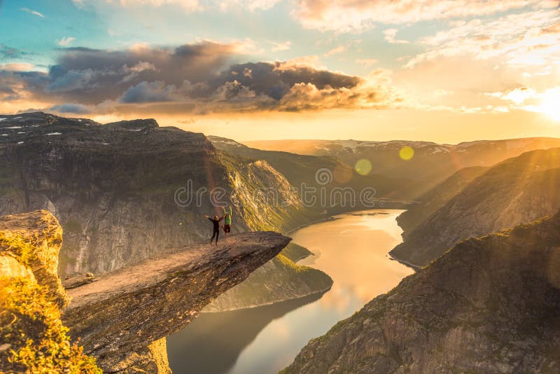 02/09-17, Trolltunga, Norway. Two women are jumping on the edge of trolltunga facing the sun. The drop down is 700 m. 02/09-17, Trolltunga, Norway. Two women are jumping on the edge of trolltunga facing the sun. The drop down is 700 m