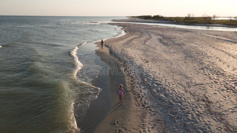 Dwie małe dziewczynki w różowych strojach pływackich biegną wzdłuż linii wodnej na pustynnej plaży. strzelanina. widok górny. dzie