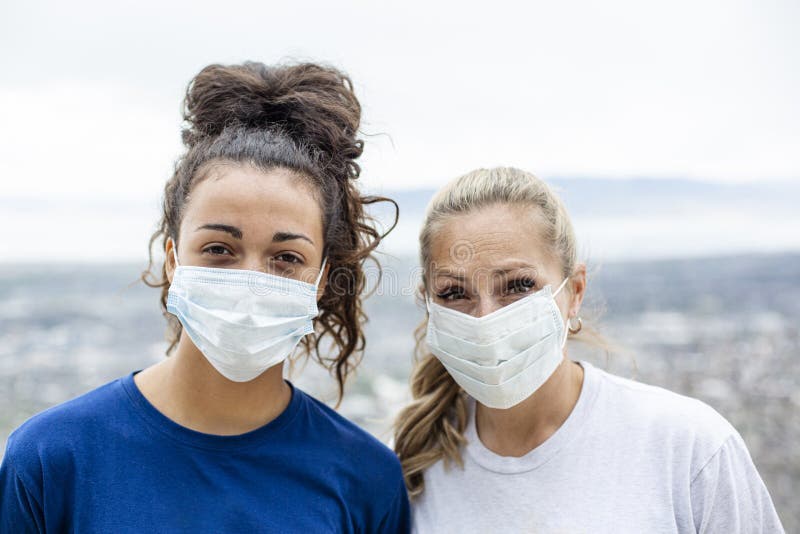 Two diverse women wearing personal protective equipment masks as they walk outdoors. Wearing essential facemasks during COVID-19 pandemic in an outdoor setting. Two diverse women wearing personal protective equipment masks as they walk outdoors. Wearing essential facemasks during COVID-19 pandemic in an outdoor setting