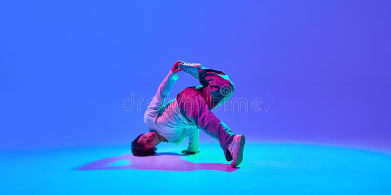 Dynamic image of energetic young guy, breakdancer in motion, performing, showing skills against gradient blue purple stock photo