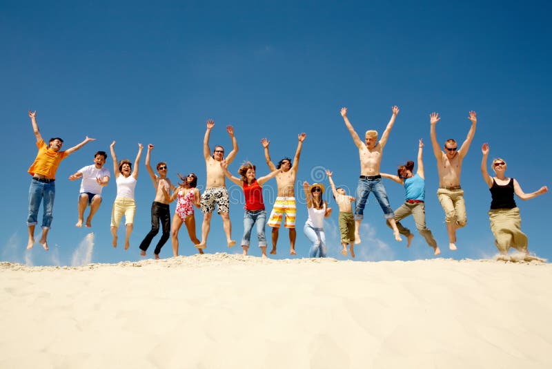 Crowd of friends jumping on sandy beach with their arms raised against blue sky. Crowd of friends jumping on sandy beach with their arms raised against blue sky