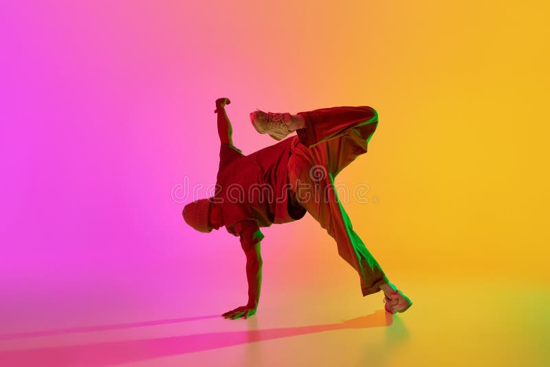 Dynamic photo of young, stylish dressed man breakdancer posing in neon light against gradient pink-yellow background. stock photography