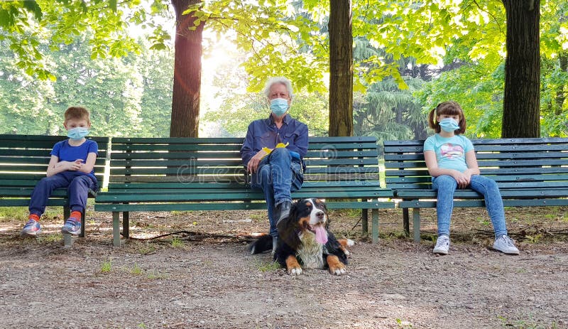 Social distancing: grandfather and grandchildren are sitting on park benches with masks during the coronavirus pandemia. Social distancing: grandfather and grandchildren are sitting on park benches with masks during the coronavirus pandemia