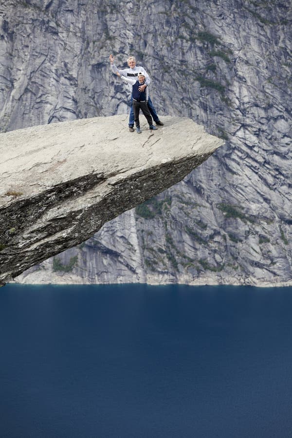 Dziad stoi na Trolltunga falezie wp?lnie z nastoletniego syna powitaniem z r?kami Macha? ich r?ki i ono u?miecha si? obrazy royalty free Dziad stoi na Trolltunga falezie wp?lnie z nastoletniego syna powitaniem z r?kami Macha? ich r?ki i ono u?miecha si? obrazy royalty free
