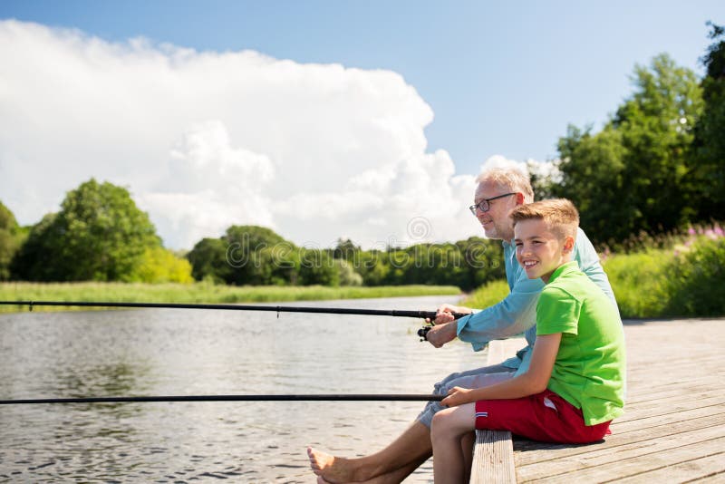 Family, generation, summer holidays and people concept - happy grandfather and grandson with fishing rods on river berth. Family, generation, summer holidays and people concept - happy grandfather and grandson with fishing rods on river berth