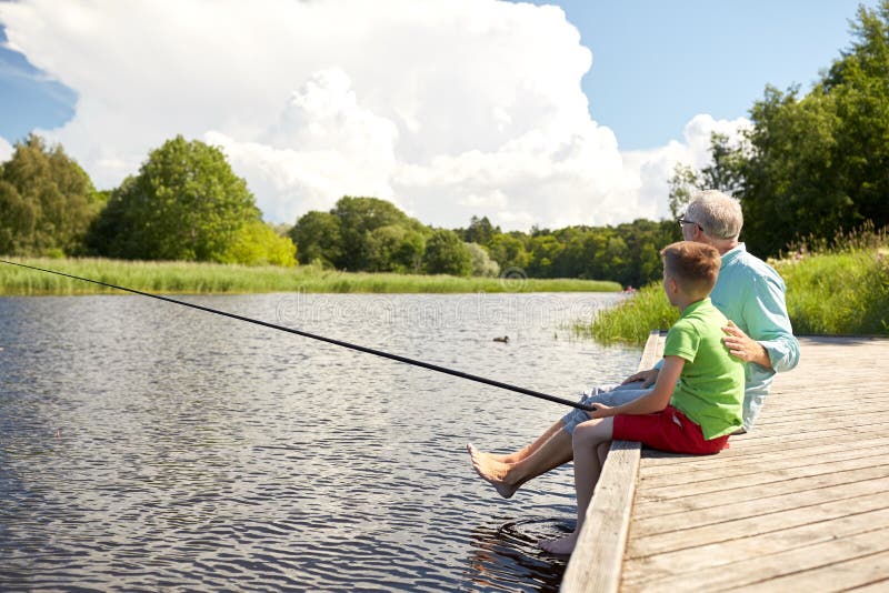 Family, generation, summer holidays and people concept - happy grandfather and grandson with fishing rods on river berth. Family, generation, summer holidays and people concept - happy grandfather and grandson with fishing rods on river berth