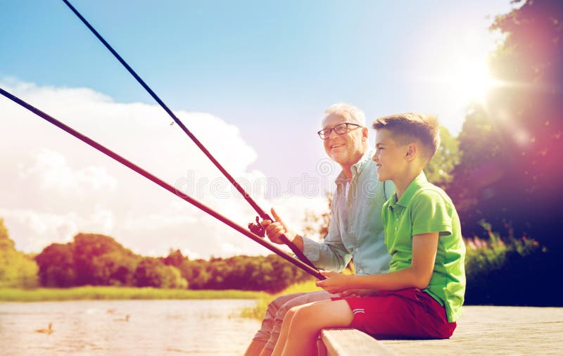 Family, generation, summer holidays and people concept - happy grandfather and grandson with fishing rods on river berth. Family, generation, summer holidays and people concept - happy grandfather and grandson with fishing rods on river berth