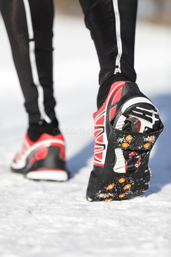 Running shoes in snow with grip soles or traction cleats with metal spikes for anti slip grip when walking or running. Man winter running in snow. Running shoes in snow with grip soles or traction cleats with metal spikes for anti slip grip when walking or running. Man winter running in snow.