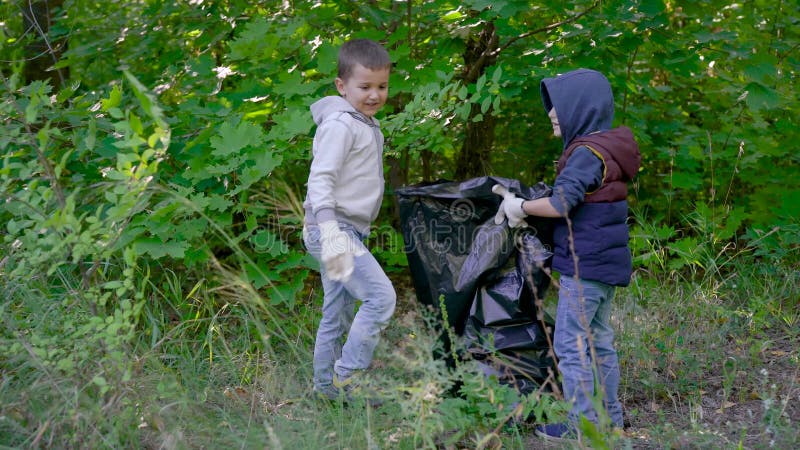 Dzieci chłopcy umieszczają śmieci z lasu w czarnej plastikowej torbie, czyszczenie wspólnego terytorium