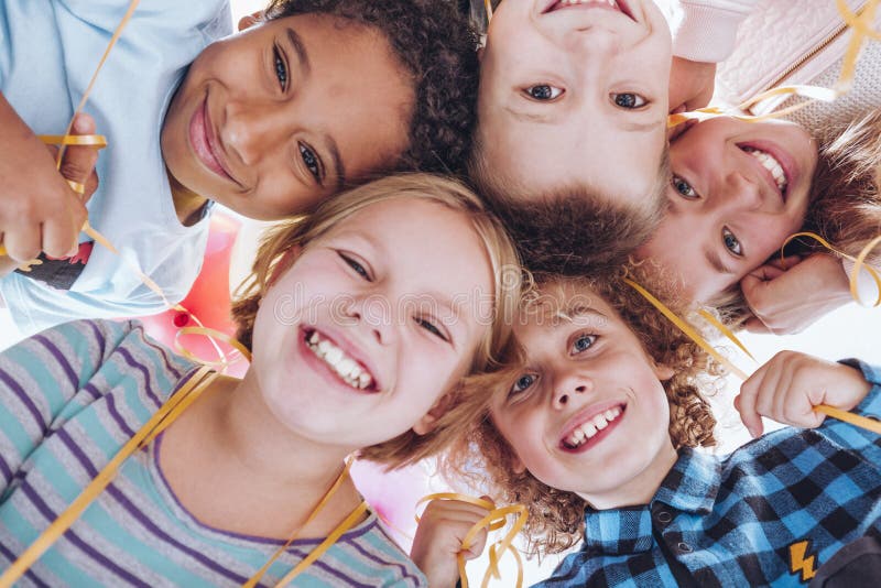 Group of smiling children holding a yellow balloon string while looking down. Group of smiling children holding a yellow balloon string while looking down