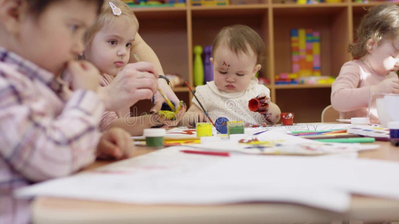 Dzieci siedzą przy stołem i remis dziecko w przedpolu rysuje używać czerwonego markiera dzieci w tle