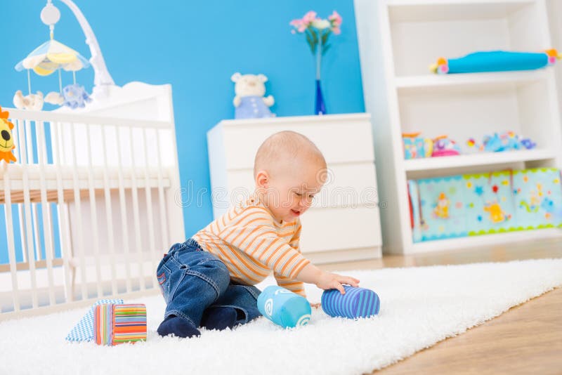 Happy baby boy (1 year old) sitting on floor at children's room and playing with toy blocks. Toys are officially property released. Happy baby boy (1 year old) sitting on floor at children's room and playing with toy blocks. Toys are officially property released.