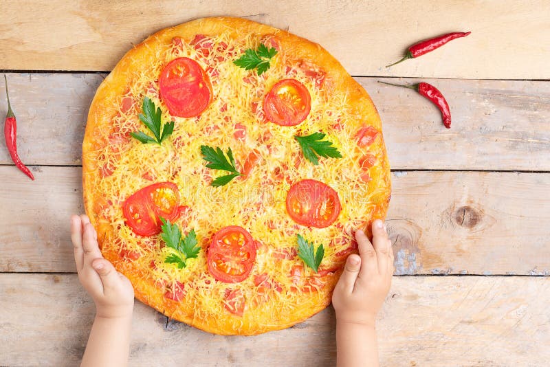 Dzieciak r?ki trzymaj? serow? margarita pizz? z pomidorami i basilem, weganinu posi?ek na drewnianym wie?niaka stole, odg?rny wid zdjęcie stock Dzieciak r?ki trzymaj? serow? margarita pizz? z pomidorami i basilem, weganinu posi?ek na drewnianym wie?niaka stole, odg?rny wid zdjęcie stock
