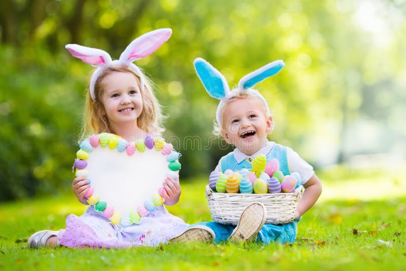 Little boy and girl having fun on Easter egg hunt. Kids in bunny ears and rabbit costume. Children with colorful eggs in a basket. Toddler kid and baby play outdoor. Blank board for your text. Little boy and girl having fun on Easter egg hunt. Kids in bunny ears and rabbit costume. Children with colorful eggs in a basket. Toddler kid and baby play outdoor. Blank board for your text.