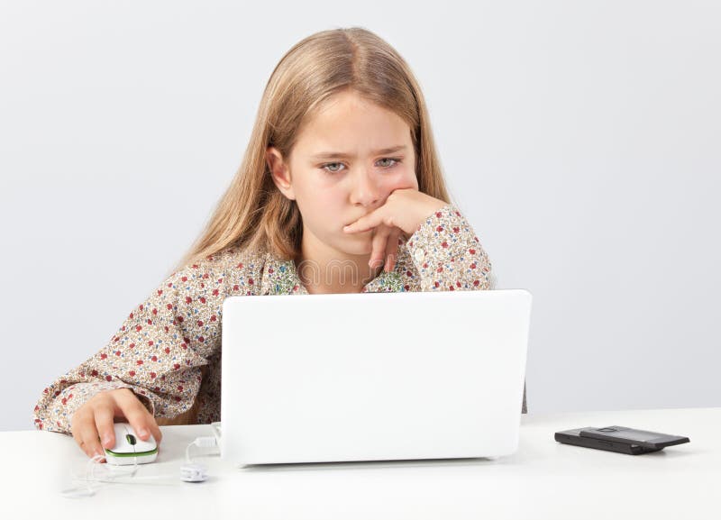 Portrait of preteen cute blond girl schoolkid sitting at desk intensively and thoughtfully watching her laptop, notebook or netbook PC screen while researching school topics on the Internet or updating Facebook. Portrait of preteen cute blond girl schoolkid sitting at desk intensively and thoughtfully watching her laptop, notebook or netbook PC screen while researching school topics on the Internet or updating Facebook.