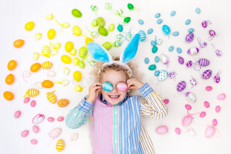 Funny little boy with bunny ears having fun on Easter egg hunt. Child playing with colorful Easter eggs. Kids play with pastel color rainbow eggs. Spring and Easter art and crafts for children. Funny little boy with bunny ears having fun on Easter egg hunt. Child playing with colorful Easter eggs. Kids play with pastel color rainbow eggs. Spring and Easter art and crafts for children.