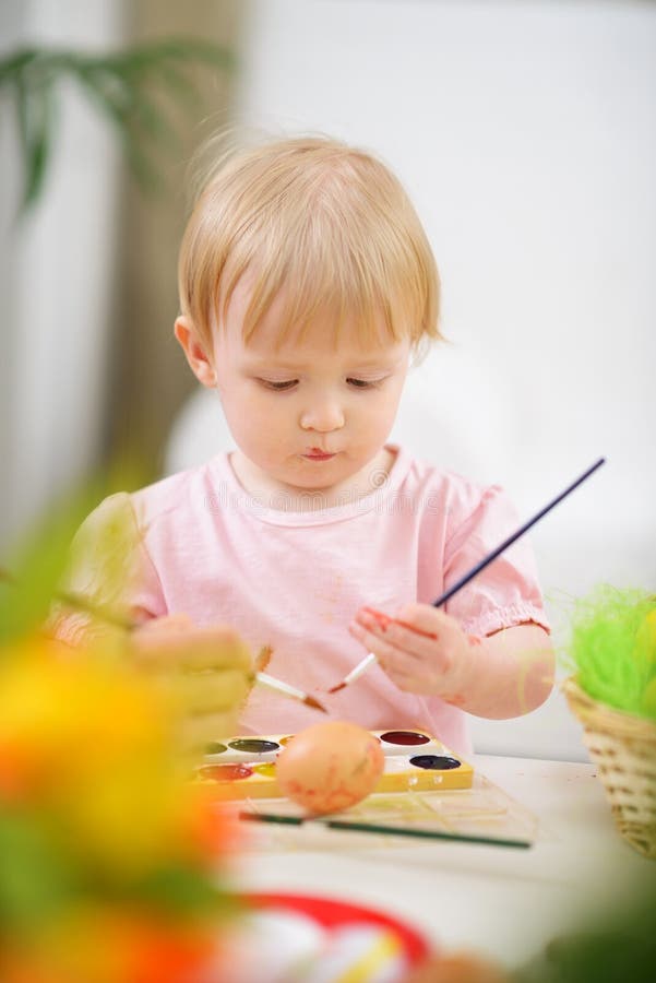 Color smeared baby girl painting Easter egg. Color smeared baby girl painting Easter egg