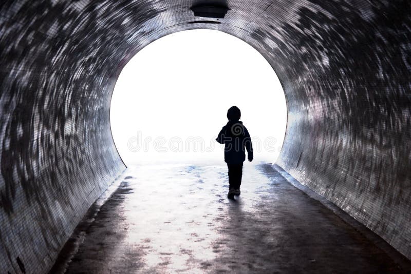 Child walking through a dark tunnel into the light at the end of it. High contrast freedom concept. Child walking through a dark tunnel into the light at the end of it. High contrast freedom concept