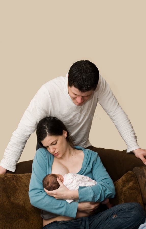 Young parents. Dad watching Mother feeding new baby. Young parents. Dad watching Mother feeding new baby