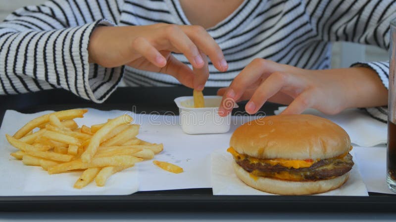 Dziecka łasowania hamburger w restauracji, dzieciak i fast food, dziewczyna Pije sok fotografia royalty free Dziecka łasowania hamburger w restauracji, dzieciak i fast food, dziewczyna Pije sok fotografia royalty free