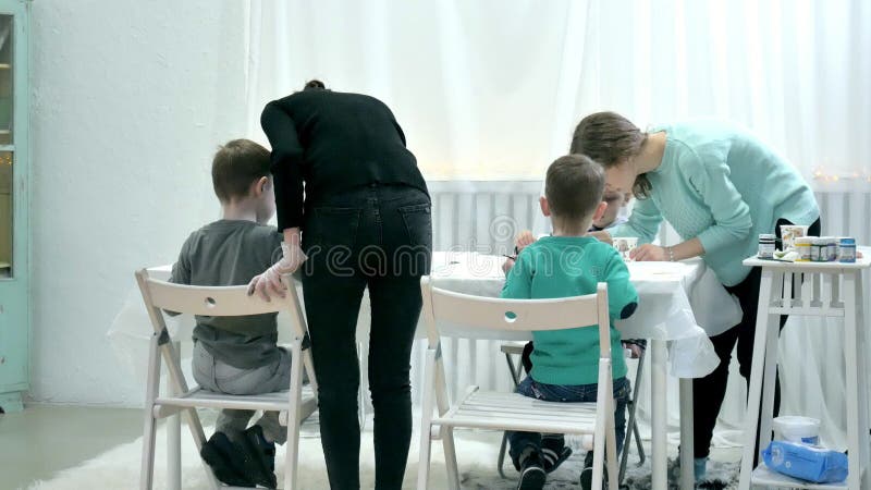 Dziecko chłopiec siedzi wpólnie wokoło stołu w sala lekcyjnej i rysunku Z one są ich piękny nauczyciel i potomstwa