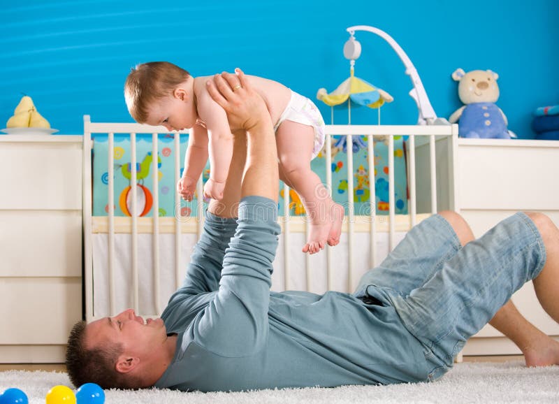 Father lying on back and lifting baby boy ( 1 year old ) at home in children's room. Father lying on back and lifting baby boy ( 1 year old ) at home in children's room.