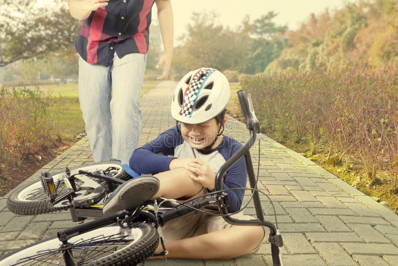 Little boy crying on the road while holding his knee after falling from the bicycle with dad on the back. Little boy crying on the road while holding his knee after falling from the bicycle with dad on the back