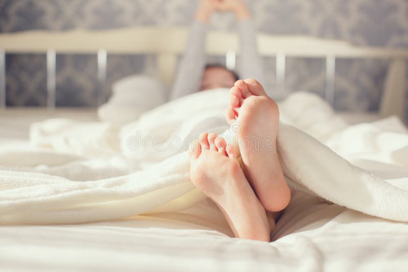 Bare feet children's feet,little girl,waking up in the morning on a big white bed in his bedroom with gray Wallpaper,girl is covered with white soft fluffy blanket,the child stretches himself,raising up his hands. Bare feet children's feet,little girl,waking up in the morning on a big white bed in his bedroom with gray Wallpaper,girl is covered with white soft fluffy blanket,the child stretches himself,raising up his hands