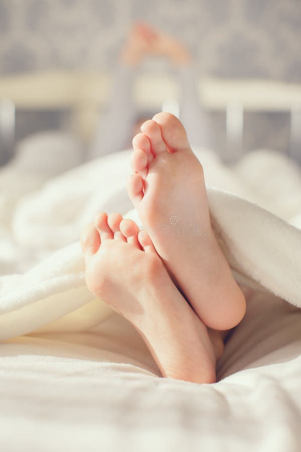 Bare feet children's feet,little girl,waking up in the morning on a big white bed in his bedroom with gray Wallpaper,girl is covered with white soft fluffy blanket,the child stretches himself,raising up his hands. Bare feet children's feet,little girl,waking up in the morning on a big white bed in his bedroom with gray Wallpaper,girl is covered with white soft fluffy blanket,the child stretches himself,raising up his hands