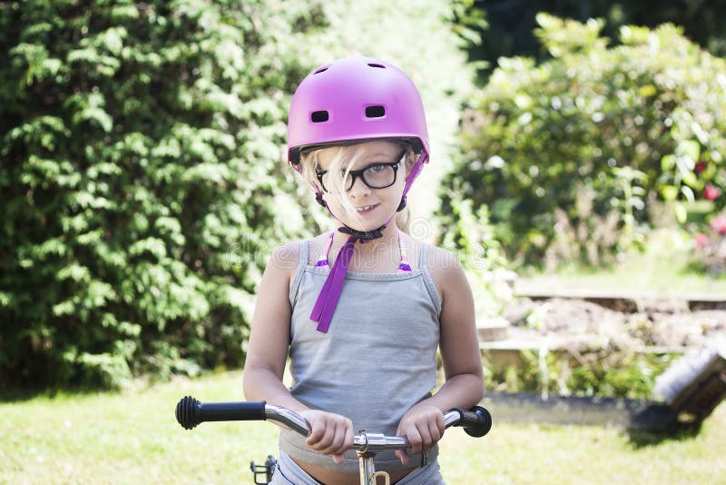 Dziecko z różowym rowerowym hełmem i czarni szkła na rowerze