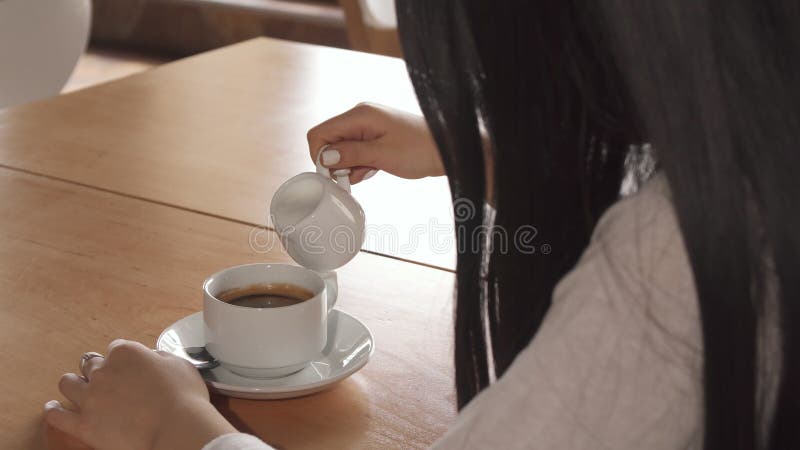 Dziewczyna dodaje śmietankę w jej kawę przy kawiarnią fotografia stock Dziewczyna dodaje śmietankę w jej kawę przy kawiarnią fotografia stock