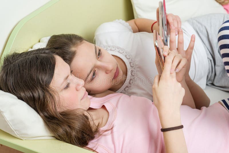 Dziewczyna nastolatkowie z interesem oglądają ich ulubionych nastoletnich seriale telewizyjnych na ich smartphone Kłamstwo w łóżk zdjęcie stock Dziewczyna nastolatkowie z interesem oglądają ich ulubionych nastoletnich seriale telewizyjnych na ich smartphone Kłamstwo w łóżk zdjęcie stock