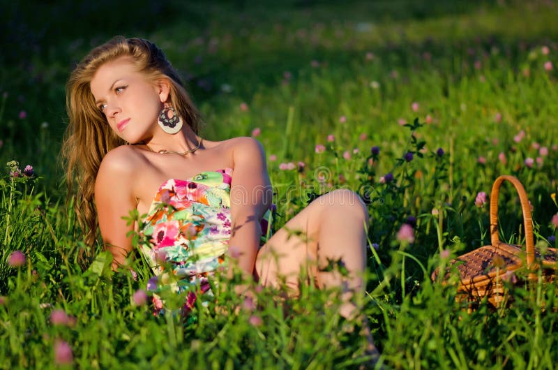 Dziewczyna siedzi w trawie z koszem na zmierzchu