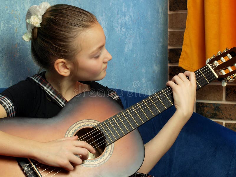 Dziewczyna w czarnej sukience z blond włosami siedzi na niebieskiej sofie na niebieskiej ścianie z brązową gitarą w rękach zdjęcia royalty free