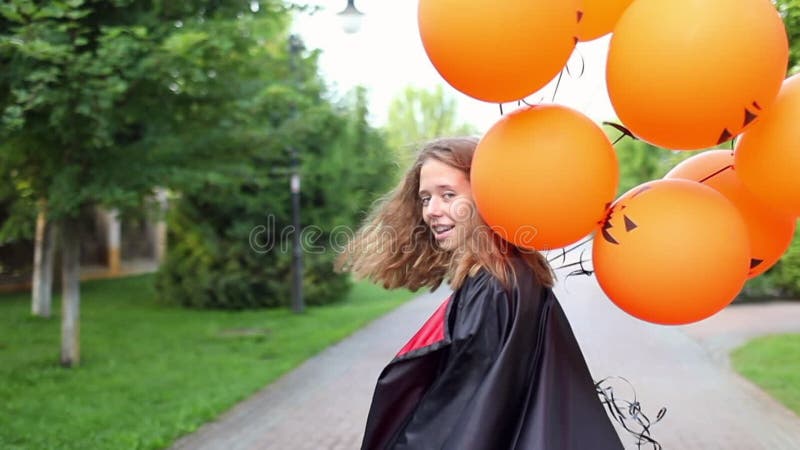 Dziewczyna w czarnym płaszczu trzymająca baloniki halloween dyni