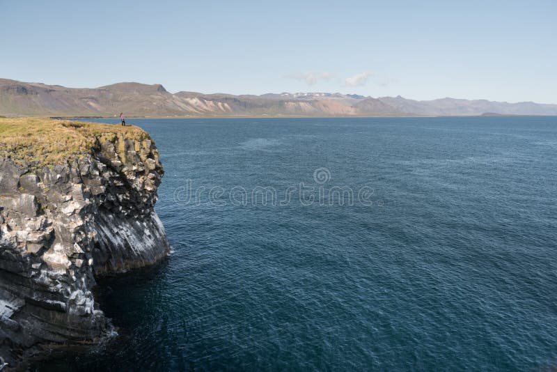 Dziewczyna w wodoodpornych kurtka stojakach na falezie na tle ocean w Iceland zdjęcie stock Dziewczyna w wodoodpornych kurtka stojakach na falezie na tle ocean w Iceland zdjęcie stock