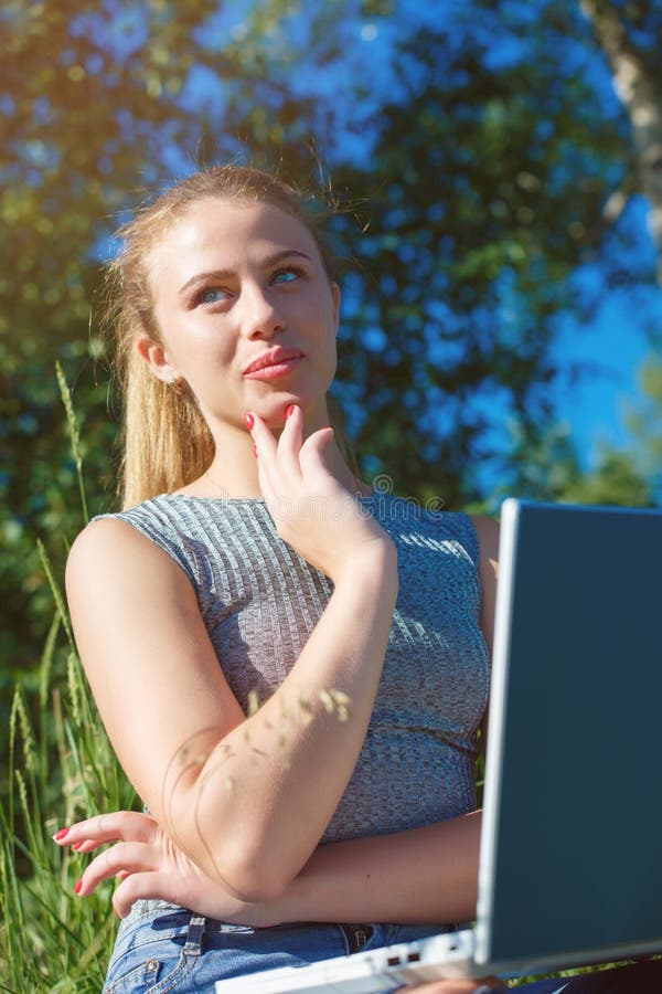 A girl with a laptop in nature among the green grass. Girl with laptop outdoors looking at the screen. A girl with a laptop in nature among the green grass. Girl with laptop outdoors looking at the screen