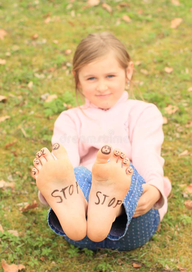 Barefoot kid - funny girl with ten smileys - small faces on toes and signs STOP on soles of her bare feet. Barefoot kid - funny girl with ten smileys - small faces on toes and signs STOP on soles of her bare feet