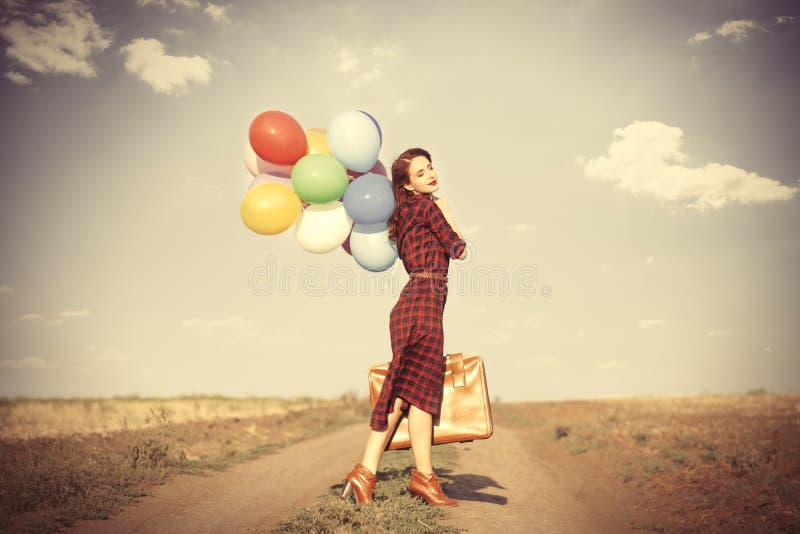 Beautiful girl in plaid dress with multicolored balloons and bag on countryside. Beautiful girl in plaid dress with multicolored balloons and bag on countryside