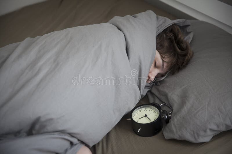 Dziewczyna, zawijaj? ca w popielatej koc, stawia za jej r? ce obraca? daleko alarm Tam s? sze?? godzin na budziku obrazy stock