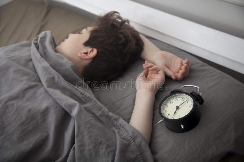 Dziewczyna, zawijaj? ca w popielatej koc, stawia za jej r? ce obraca? daleko alarm Tam s? sze?? godzin na budziku zdjęcie royalty free