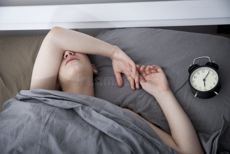 Dziewczyna, zawijaj? ca w popielatej koc, stawia za jej r? ce obraca? daleko alarm Tam s? sze?? godzin na budziku zdjęcia stock