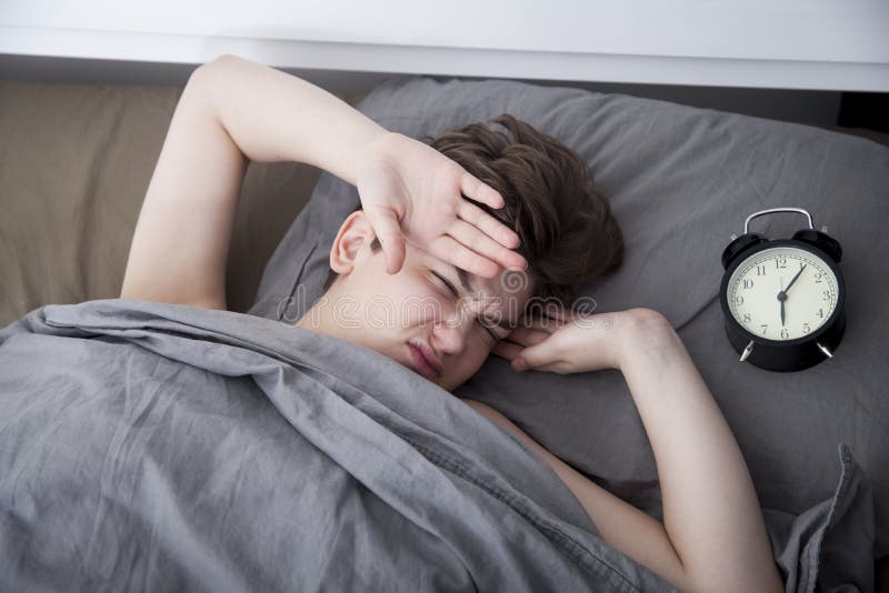 Dziewczyna, zawijaj? ca w popielatej koc, stawia za jej r? ce obraca? daleko alarm Tam s? sze?? godzin na budziku zdjęcie stock