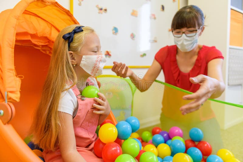 Toddler girl in child occupational therapy session doing playful exercises with her therapist during Covid - 19 pandemic, both wearing protective face masks. Toddler girl in child occupational therapy session doing playful exercises with her therapist during Covid - 19 pandemic, both wearing protective face masks