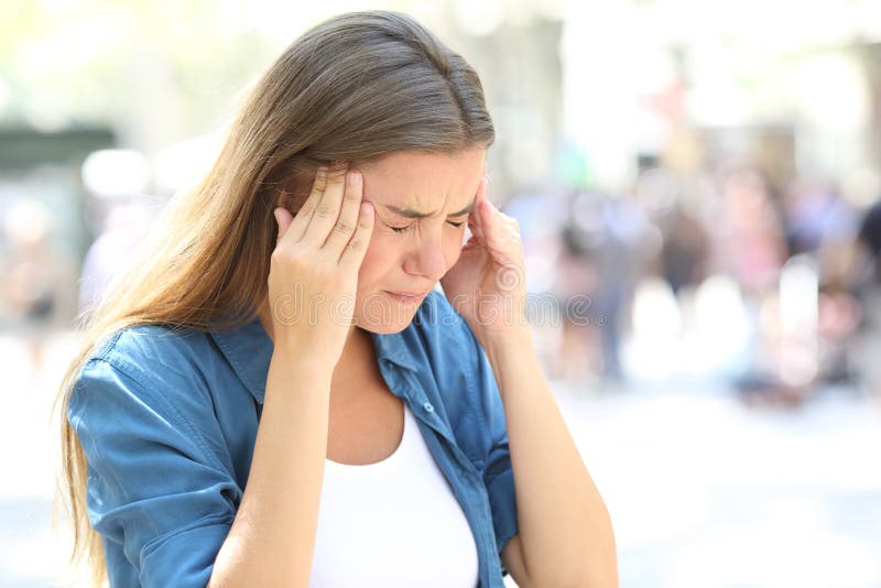 Painful girl suffering migraine touching temple in the street. Painful girl suffering migraine touching temple in the street