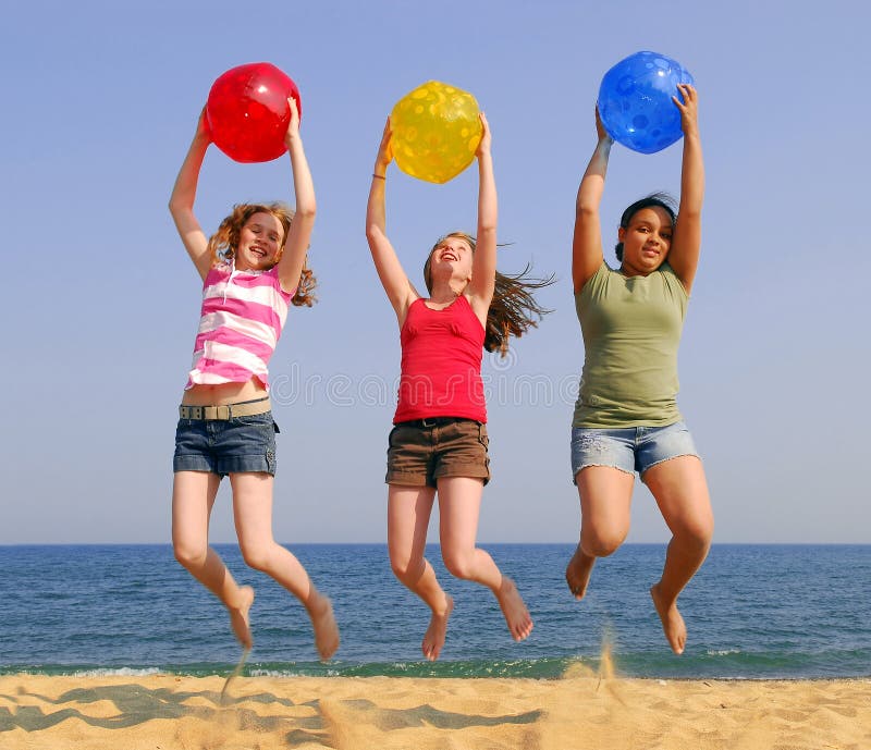 Three girls on a sandy beach jumping with colorful balls. Three girls on a sandy beach jumping with colorful balls